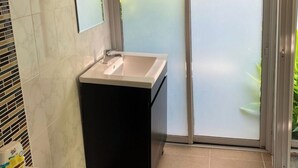 A bathroom with a white sink, black cabinet, and a large window with frosted glass.