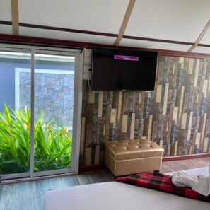 Ein Hotelzimmer mit einer Schiebetür zu einem Balkon, einem flachbildfernseher an der Wand, einer gepolsterten Lederbank und einem Bett mit rot-schwarzem Schachbrettmusterdecke.