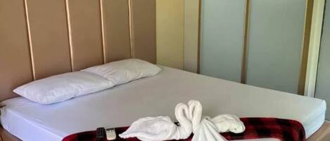 A neatly made bed with white linens and a red and black checkered blanket, a white pillow, and a swan-shaped towel arrangement.