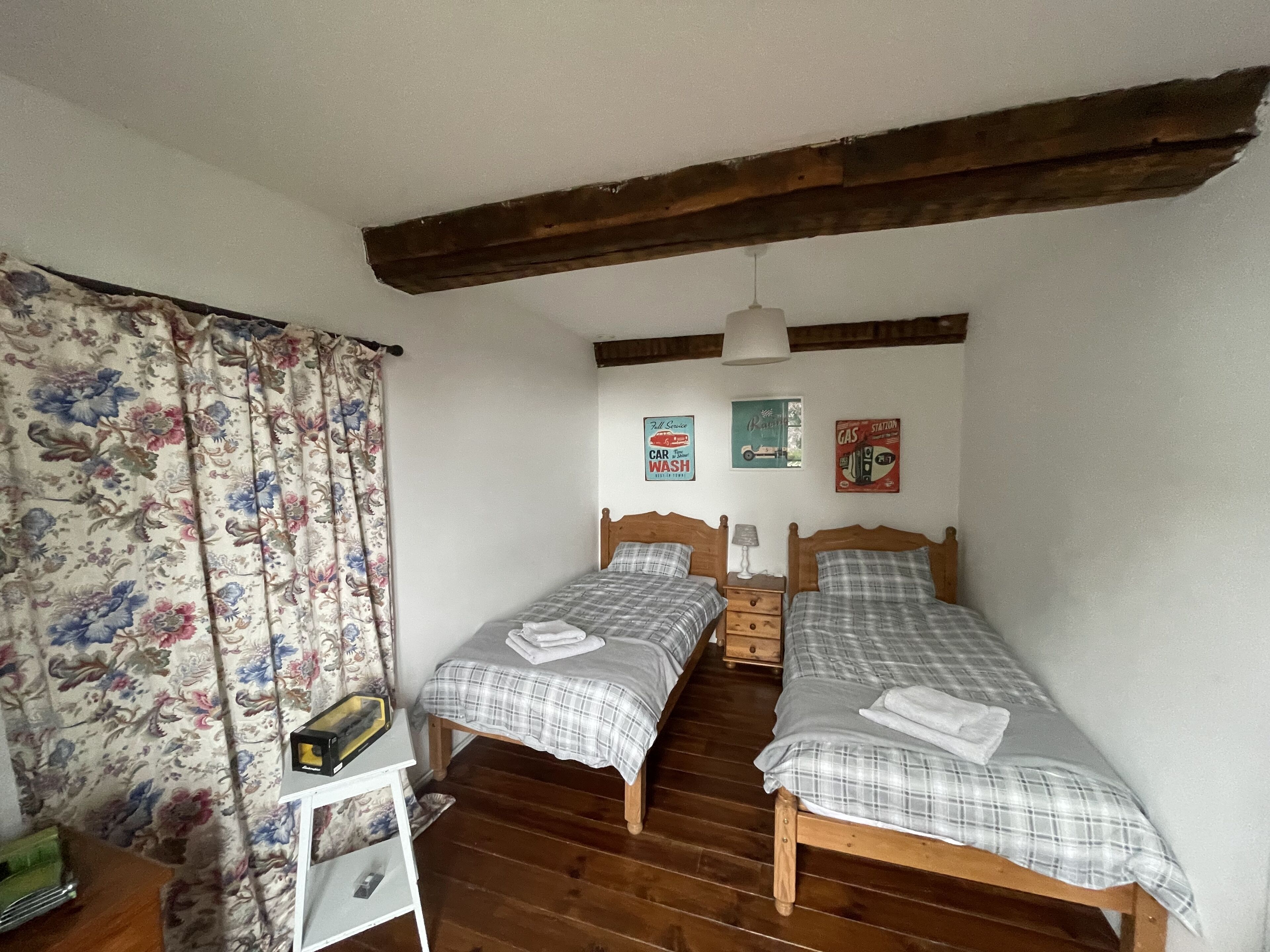 Camera da letto con due letti di legno, un tavolino e tende floreali.