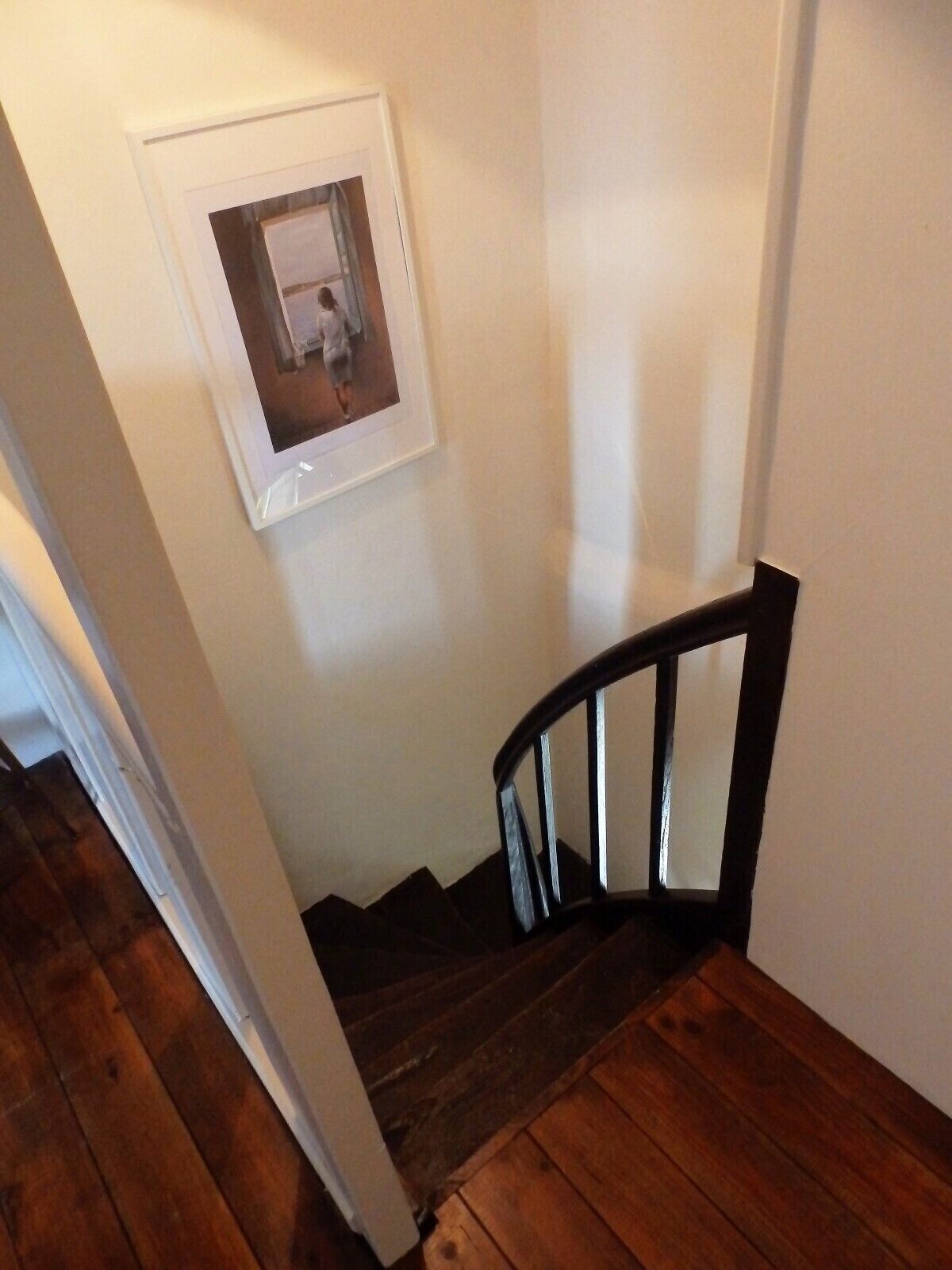 Un escalier en bois à la teinte foncée, des murs blancs et un tableau encadré accroché au mur.