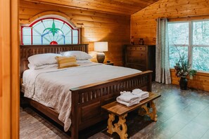 Une pièce en bois comprenant un lit, une table de chevet, une commode, une fenêtre avec des rideaux et une fenêtre en vitrail située au-dessus du lit.