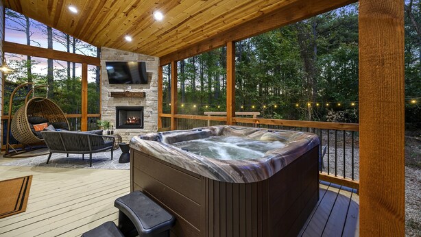 A wooden deck with a hot tub, a stone fireplace, and a hanging chair.