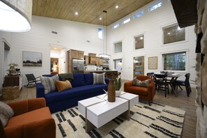 A spacious living area with a blue sofa, orange armchair, and a white coffee table. A kitchen with wooden cabinets and a dining area with a table and chairs are visible.