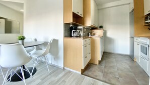 Een moderne keuken met witte kastjes, een houten aanrechtblad en een eethoek met een witte tafel en stoelen.
