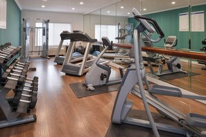 Una palestra con diverse attrezzature per l'allenamento, tra cui tapis roulant, ellittiche e pesi liberi.