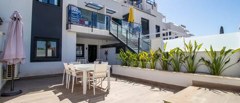 A modern building with a balcony, outdoor seating, and potted plants.