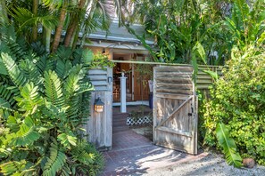 A wooden gate leading to a house with a porch, surrounded by lush greenery.
