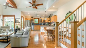 A spacious living room with a sofa, a dining area with chairs, wooden flooring, and a staircase with wooden railings.