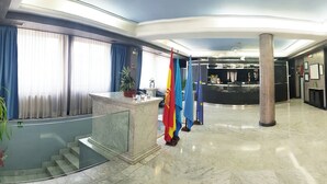 Un vestíbulo con suelo de mármol, mostrador de recepción, escalera y banderas.