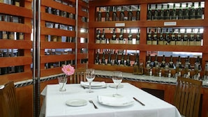 Un restaurante con una mesa blanca dispuesta para dos, rodeada de estantes llenos de botellas de vino.