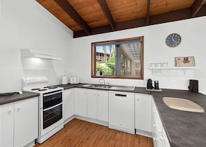 A modern kitchen with white cabinets, a built-in oven, a sink, and a window with a view of greenery.