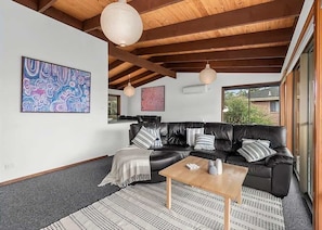 A modern living room with a black leather sofa, a wooden coffee table, and abstract art on the walls.