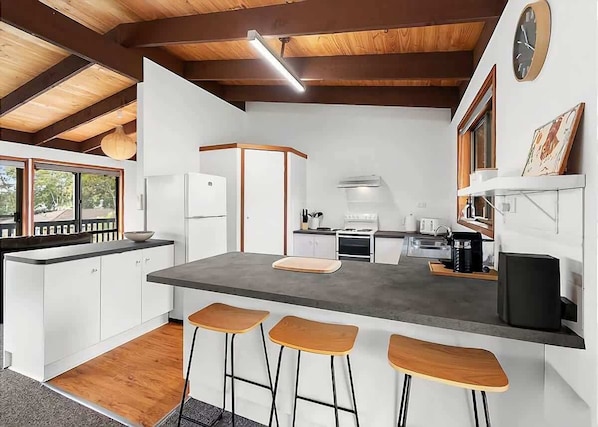 A modern kitchen with white cabinets, a grey countertop, wooden stools, and a large window.
