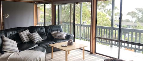 A modern living room with a black leather sofa, a wooden coffee table, and a large window offering a view of the outdoors.
