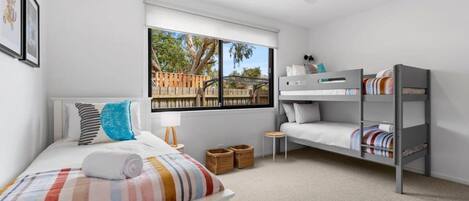 A bedroom with a bed, a window, a bunk bed, a ceiling fan, and a view of the outside.