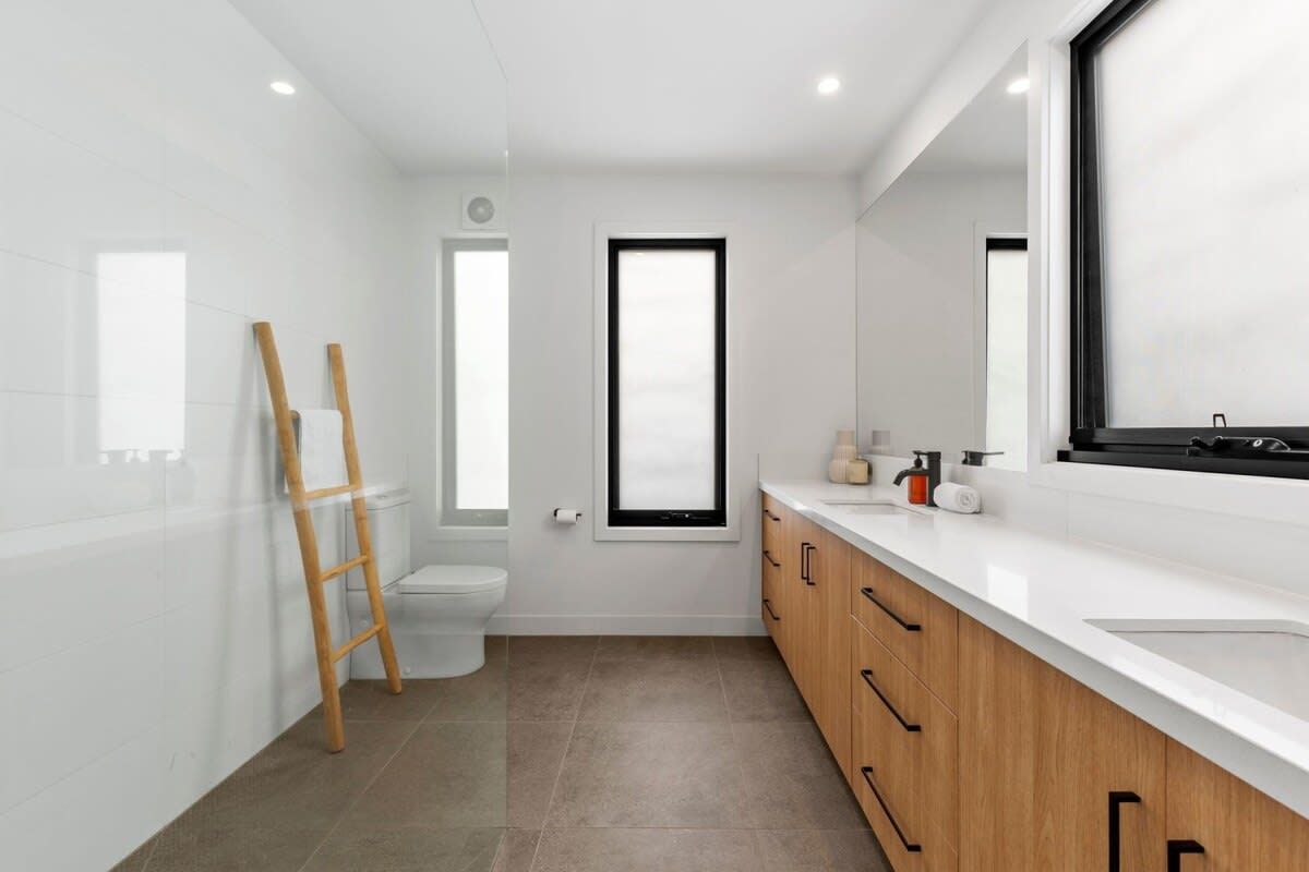 A modern bathroom with a toilet, a window, a sink, and a mirror.