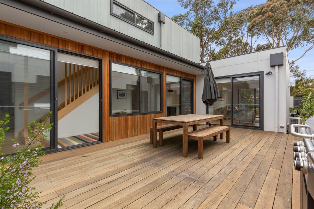A modern house with a wooden deck, a dining table, and a barbecue grill.