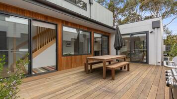 A modern house with a wooden deck, a dining table, and a barbecue grill.