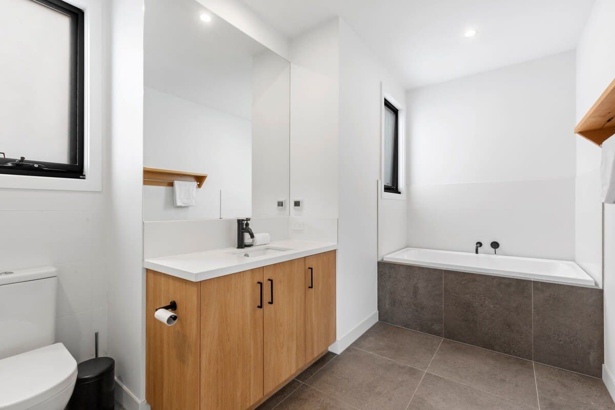 A modern bathroom with a toilet, sink, mirror, and bathtub.