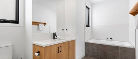 A modern bathroom with a toilet, sink, mirror, and bathtub.