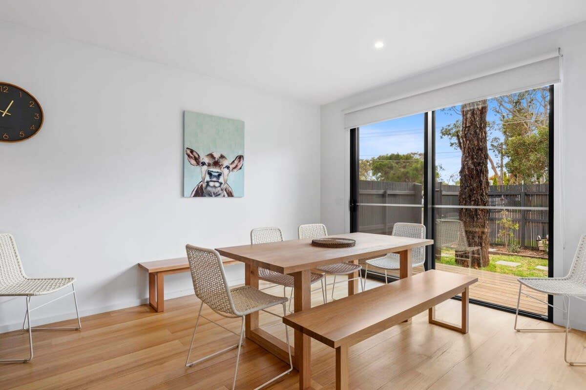A modern dining area with a wooden table, woven chairs, and a large window with a view of the outdoors.