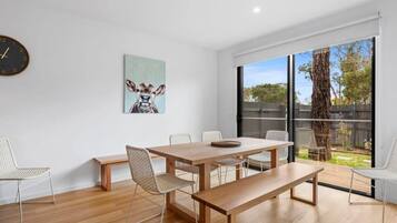 A modern dining area with a wooden table, woven chairs, and a large window with a view of the outdoors.