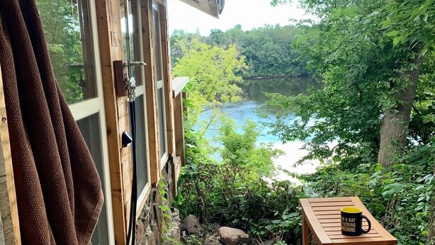 A wooden deck leading to a cabin with a view of a lake surrounded by trees. - Tiny rustic cabin next to the Mississippi River  (St. Cloud)