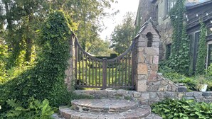 A stone staircase leading to a gated entrance surrounded by lush greenery and a stone building. - Tiny rustic cabin next to the Mississippi River  (St. Cloud)