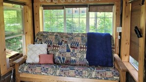 A wooden cabin interior with a patterned sofa, a window with a view of greenery, and a ceiling with a butterfly design. - Tiny rustic cabin next to the Mississippi River  (St. Cloud)