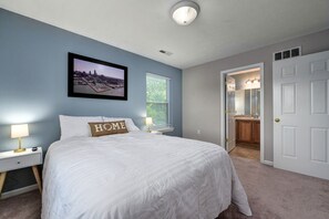 A bedroom with a bed, a nightstand, a lamp, a framed cityscape picture, and a door leading to a bathroom. - Cozy Ohio City home w/Hot Tub & amazing amenities! (Cleveland)