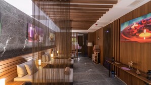 Un moderno vestíbulo de hotel con un mostrador de recepción de madera, una zona de estar con cojines, un panel decorativo y un cuadro grande en la pared.