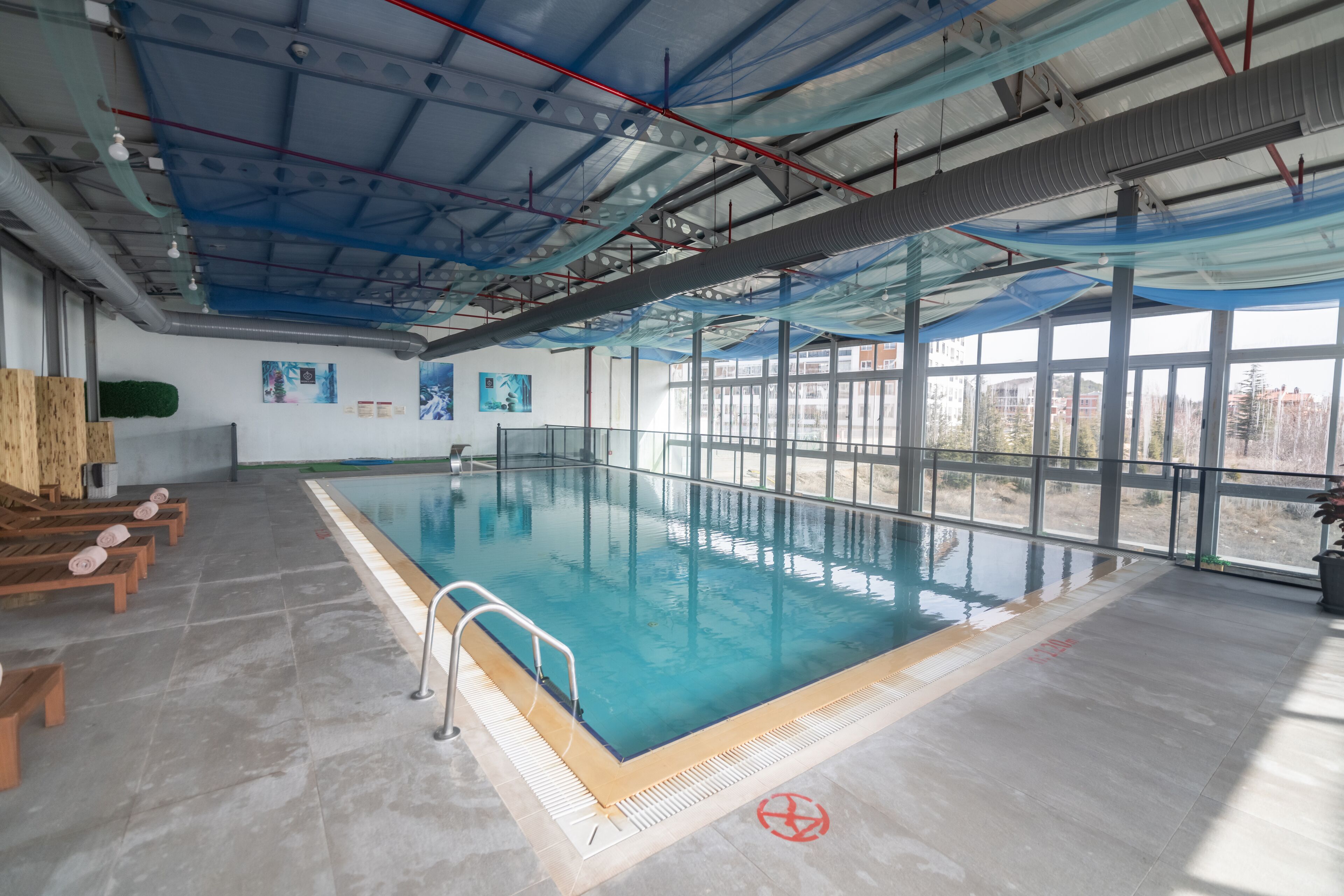 Una piscina interior amb parets de vidre transparent, gandules de fusta i un paviment de rajoles.