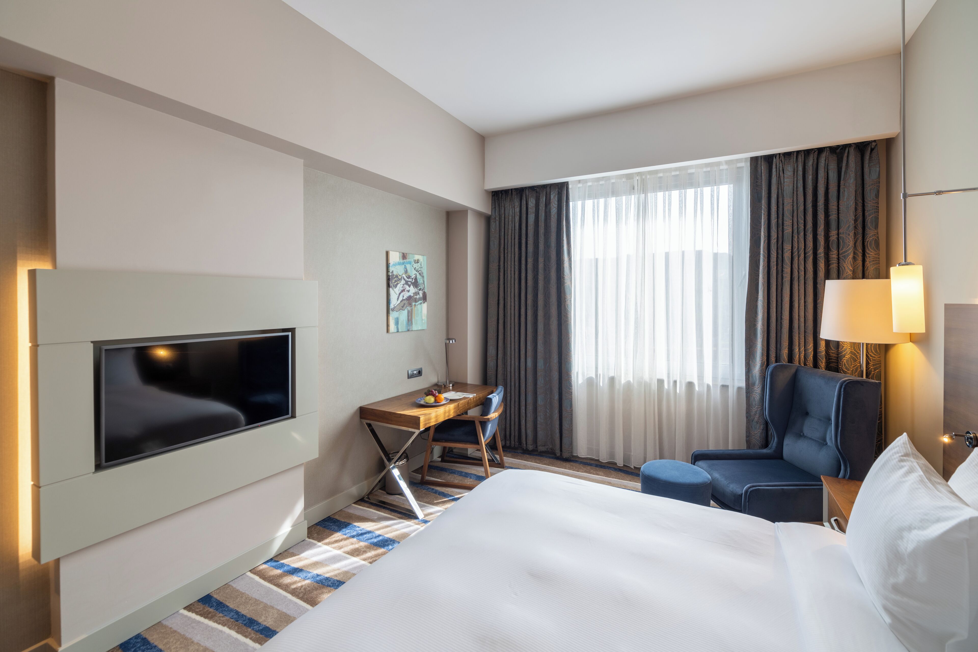 Ein Hotelzimmer mit einem Bett, einem Schreibtisch mit Stuhl, einem Fernseher und einem Fenster mit Vorhängen.