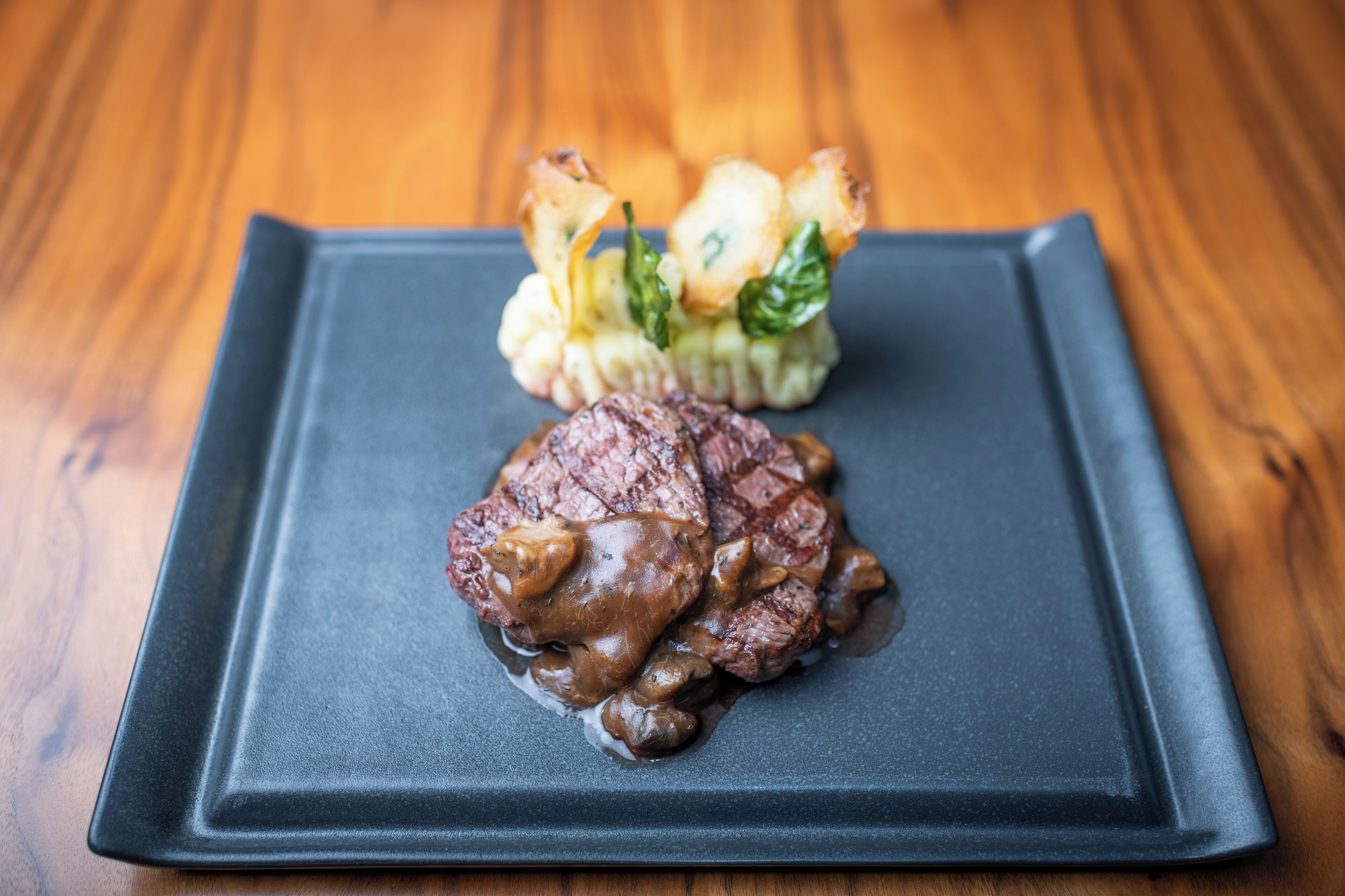 Een vierkant bord met een steak en groenten op een houten tafel.