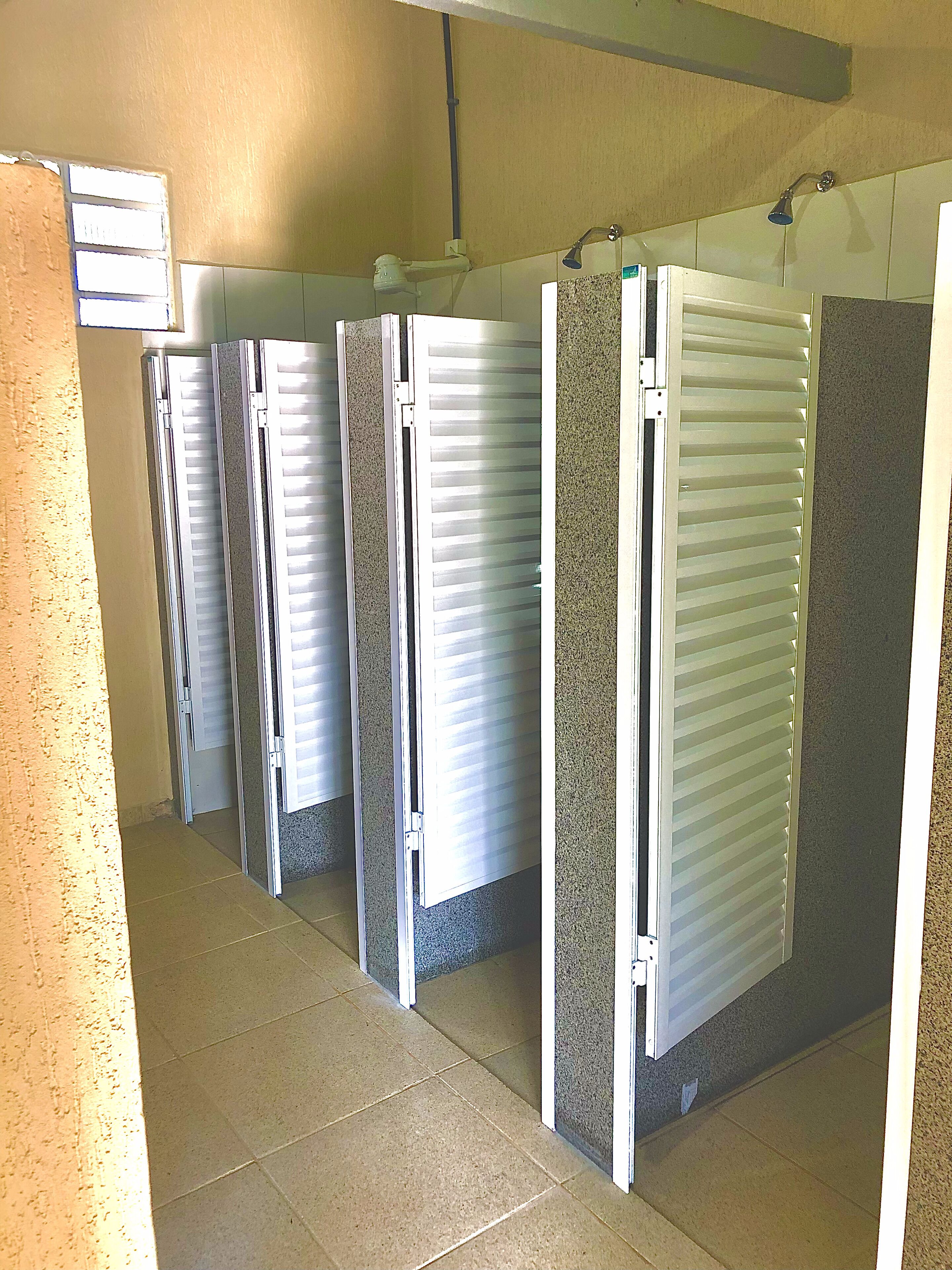 Una fila de cabinas de ducha individuales con puertas blancas y suelo de baldosas.