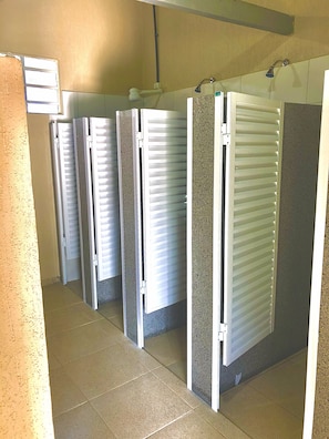A row of individual shower stalls with white doors and a tiled floor. - Family Camp (Suzano)