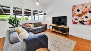 Uma sala de estar moderna com um sofá cinzento, uma televisão e uma janela grande.