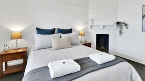 Quarto de hotel bem arrumado com uma cama, duas mesas de cabeceira, uma prateleira fixada na parede com uma planta e uma lareira.