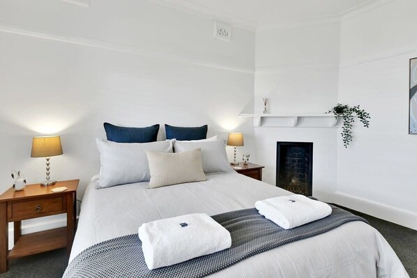 A neatly arranged hotel room with a bed, two bedside tables, a wall-mounted shelf with a plant, and a fireplace.