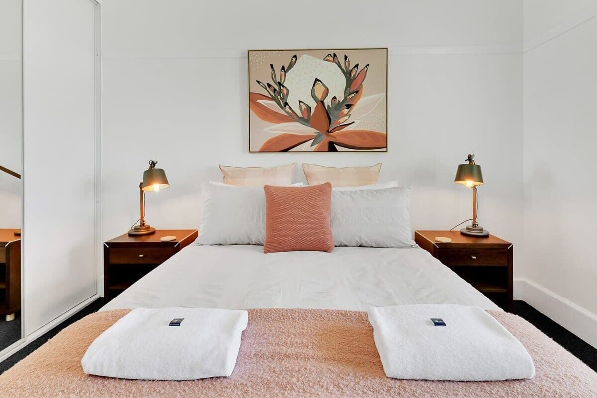 A hotel room with a bed, two bedside tables, a wall-mounted artwork, and two white towels on the floor.