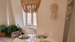 Un coin repas avec une table ronde dressée pour quatre personnes, des chaises blanches et un luminaire suspendu.