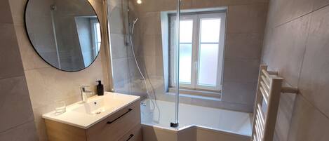 Un baño moderno con bañera, un espejo redondo, un lavabo y una ventana que deja entrar luz natural.