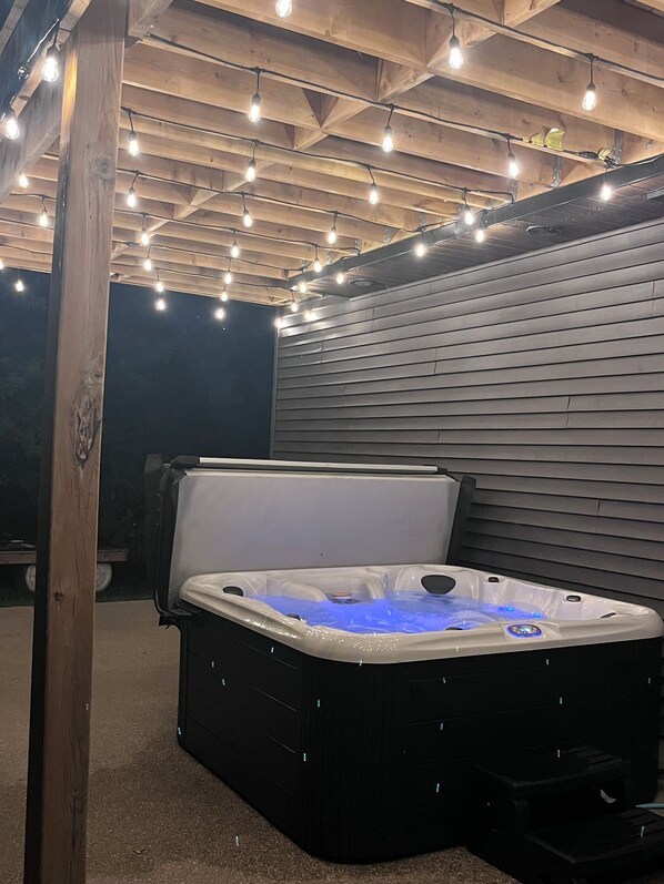 A hot tub under a wooden ceiling with string lights.