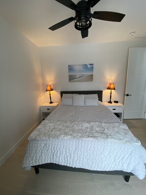 A bedroom with a bed, two bedside tables, a ceiling fan, and a wall-mounted picture.
