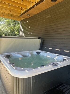 A hot tub with multiple jets, surrounded by a wooden deck and a pergola.