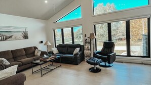 Ein geräumiges Wohnzimmer mit großem Fenster, einer Couch, einem Sessel und einem Couchtisch.