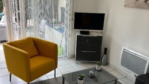 En moderne stue med en gul lænestol, en grå sofa, et fladskærms-tv og et lille sofabord med dekorative genstande.
