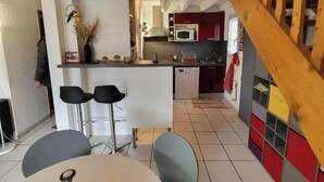 Et rummeligt køkken med en trætrappe, et spiseområde med et rundt bord og to stole, samt udsigt til opholdsstuen.