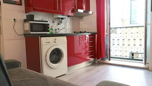 Une cuisine de taille réduite équipée d’un lave-linge, d’un four à micro-ondes et de meubles de rangement rouges.